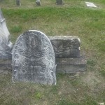 Grave marker of John and his wife, featuring their names and dates, surrounded by flowers and greenery
